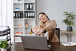 © amnaj - Asian businesswoman doing office stretches at her desk, feeling relaxed during a busy workday or break