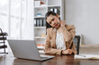 © amnaj - Asian businesswoman suffering from neck pain at her office desk, holding her sore neck while working on a laptop