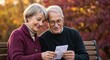 © Svetlana - Happy senior couple checking a receipt while sitting on a park bench. Elderly man and woman reviewing their finances together in autumn. Retirement planning and budgeting concept