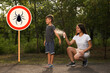 © New Africa - Woman applying insect repellent on her son's arm in park near tick warning sign