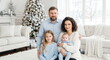 © mashimara - A Family Holiday Portrait: A heartwarming portrait of a family of four, adorned with festive attire, smiles amidst the backdrop of a beautifully decorated Christmas tree.