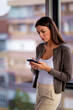 © gzorgz - Stressed business woman standing in a moder office and using her smartphone