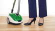 © Cantarela - Woman in high heels standing with a vacuum cleaner on a wooden floor. Housekeeping concept for modern domestic life.