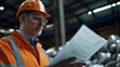© A2Z AI  - A construction worker reviews plans at a factory.  He is wearing a hard hat, safety glasses and an orange reflective vest. The worker is focused on the task at hand.