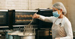 © peopleimages.com - Mask, baker or frying donuts in kitchen for dessert production, baking process or catering. Hospitality industry, mature person and lunch snack preparation in bakery for gastronomy or culinary safety