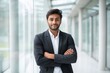 © Yuliia Malovana - Portrait of young businessman standing with arms crossed in a bright corporate office hallway, looking confident at camera, professional in business suit.