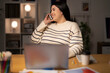 © Studio Marmellata - Young Positive female remote employee in casual clothes speaking via smartphone with client while working on project remotely using laptop