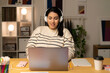 © Studio Marmellata - Young Arab female remote worker in casual wear and headphones using laptop while working online on business project sitting at table