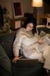 © Studio Marmellata - Concentrated Arab female in casual beige outfit and eyeglasses sitting on sofa with documents using laptop while working online at home