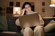 © Studio Marmellata - Arab female freelancer in casual wear and glasses typing information on laptop while working remotely sitting on sofa at home in evening