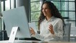 © Yuliia - Hispanic business woman office worker talking video call with computer businesswoman showing with hands gesture explain work task e-learning talk conference online distant communication female girl