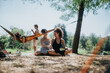 © qunica.com - Two women sit on a blanket, chatting and smiling as friends relax in a sunny park. A hammock and trees frame a casual, joyful outdoor gathering full of warmth and connection.