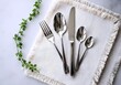 © Shawkat Hayat - Elegant polished silverware set including fork knife and spoons arranged on a textured white napkin with green vine accent