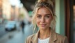 © miss irine - Young woman with blonde hair, green eyes smiles outdoors on city street. Wears tan blazer over white shirt, hair in messy bun. Natural light illuminates freckled face, conveying friendly,