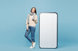 © ViDi Studio - Full body young woman wears sweater scarf point on big huge blank screen mobile cell phone isolated on plain blue background studio. Healthy lifestyle ill sick disease treatment cold season concept.