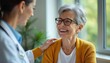 © miss irine - Doctor comforts senior woman during consultation. Healthcare pro supports elderly patient in office. Kind physician offers caring hand on shoulder of happy senior woman. Doctor smiles with trust.