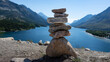 © Connect Images - A stack of balanced stones on a hill overlooking a serene lake with mountains in the background. Waterton Park, Alberta, Canada