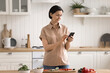 © fizkes - Middle aged woman using mobile phone standing by kitchen table
