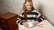 © Mariia - Smart little girl sitting on table at home drawing, cute small kid painting picture with colorful pencils.