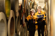 © Montri - Industrial workers inspecting large metal coils in warehouse aisle. Wearing safety uniforms and helmets. material stock check, factory inventory, manufacturing. engineer, two worker. logistics.