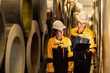 © Montri - Industrial workers inspecting large metal coils in warehouse aisle. Wearing safety uniforms and helmets. material stock check, factory inventory, manufacturing. engineer, two worker. logistics.