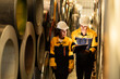 © Montri - Industrial workers inspecting large metal coils in warehouse aisle. Wearing safety uniforms and helmets. material stock check, factory inventory, manufacturing. engineer, two worker. logistics.