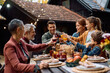 © Drazen - Happy multi-generation family celebrating Thanksgiving and toasting during meal on patio.