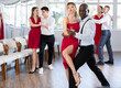 © JackF - Graceful duet, expressive African American man in formal wear and slender woman in vibrant red dress, engrossed in passionate tango during group dance class in choreographic studio..