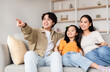 © Prostock-studio - A young family sits together on the sofa, watching a movie. The brother points at the screen while his sister and mother smile, creating a joyful atmosphere in their living room.