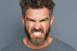 © RISHAD - Angry young man with beard showing gritted teeth on gray background