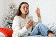 © Pixel-Shot - Beautiful young woman with mobile phone blowing kiss and sitting on sofa in living room. Christmas celebration