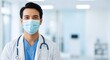 © Wool World - Smiling Asian male doctor wearing a protective face mask and stethoscope in a modern hospital setting