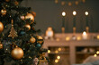 © Seventyfour - Christmas tree decorated with gold ornaments and lights standing in foreground, blurred background showing glowing candles and festive decorations creating holiday ambiance