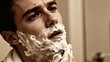 © Bay - Young man shaving with foam on his face in bathroom mirror