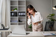 © Wasana - Asian businesswoman talking on phone and working on laptop in office