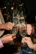 © Seventyfour - Diverse group of young adult hands clinking champagne glasses in front of decorated Christmas tree, celebrating festive occasion with sparkling wine