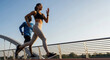 © Khasani - Side view of a fit athletic couple running outdoors on a bridge during a sunny day