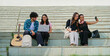 © Raushan_films - Indian young adult gen z man male woman use laptop look screen check online e work study place teen two girl sitting on stair hold mobile phone take selfie do funny pose talk enjoy break day time