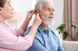 © New Africa - Caregiver helping senior man to put in hearing aid at home