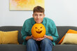 © New Africa - Halloween celebration. Man holding pumpkin with carved spooky face on sofa at home