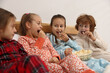 © New Africa - Cute children in pajamas eating popcorn while watching movie on bed at home