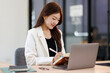 © David - Smiley young business asian woman holding business plan note and sitting at desk in modern coworking office.