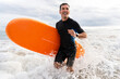 © oneinchpunch - Middle aged sportive handsome man learning surfing and running in the waves holding board