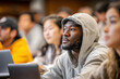 © Iryna - Close-up young black male student light hoodie intently listening lecturer lecture multinational university classroom