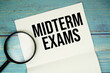 © may1985 - Midterm Exams text written on notepad with magnifying glass flat lay on wooden background
