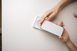 © dikushin - Close-up of female hands unboxing modern smartphone, revealing sleek device on minimalist white table, displaying anticipation during initial technology reveal. Concept of smartphone unboxing process