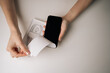 © dikushin - High-angle view of woman unpacking new smartphone and removing screen protector sitting on table, with charging cable in box visible in background. Concept of excitement of unboxing new device