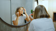 © tol_u4f - Elderly woman applying skincare products while looking in the mirror in a modern bathroom during the day