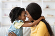 © Prostock-studio - A young girl and her mother embrace affectionately while sitting on a couch. They smile and lean their foreheads together, enjoying a warm family moment in their cozy living room.