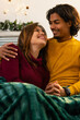 © Wavebreak Media - Diverse couple snuggling under green blanket on couch by fireplace mantel with garland and baubles